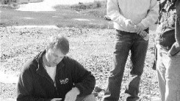 Ken Lapierre, Mustang Minerals' vice-president of exploration, kneeling (on waste rock from the Maskwa open pit) and James Moon, Senior Investment advisor with Standard Securities. The flooded ramp of the former Maskwa open pit is in the background.